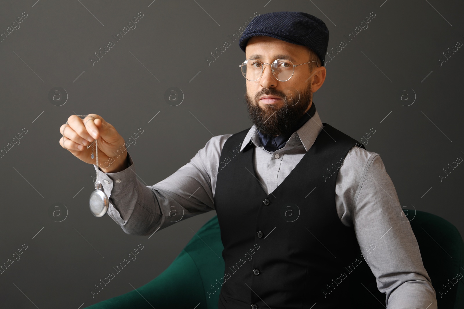 Photo of Hypnosis session. Man with vintage pocket watch in armchair near grey wall indoors