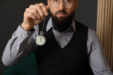 Photo of Hypnosis session. Man swinging vintage pocket watch indoors, closeup