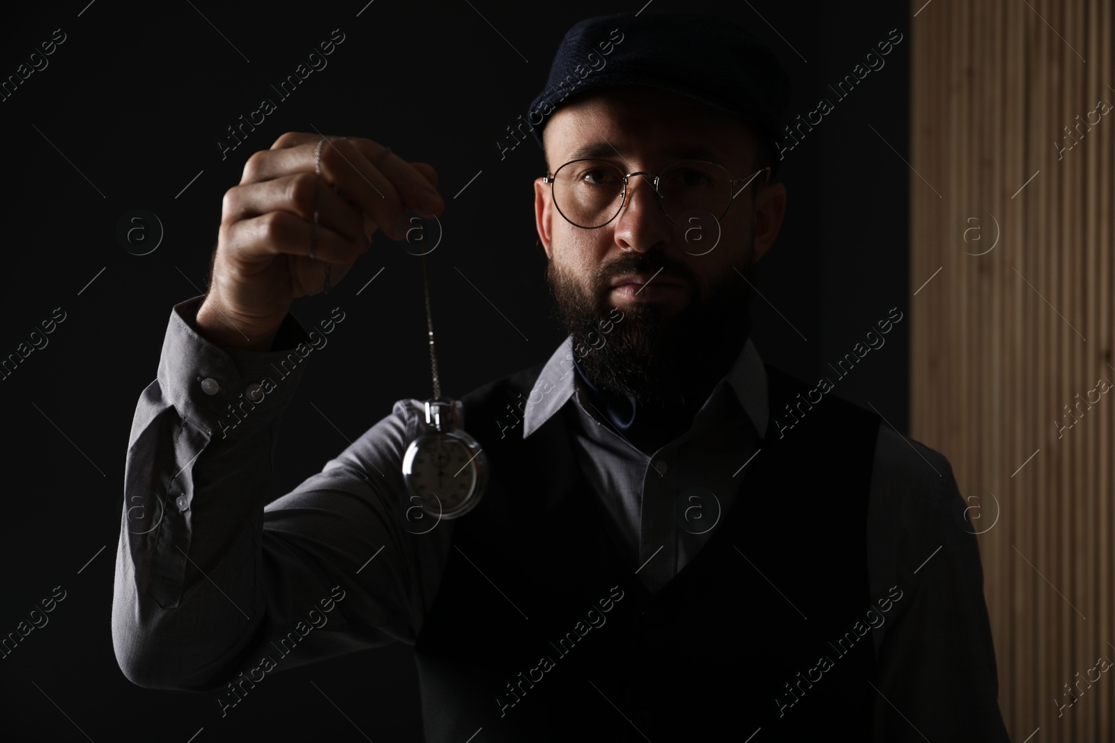 Photo of Hypnosis session. Man swinging vintage pocket watch indoors