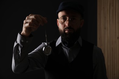 Photo of Hypnosis session. Man swinging vintage pocket watch indoors