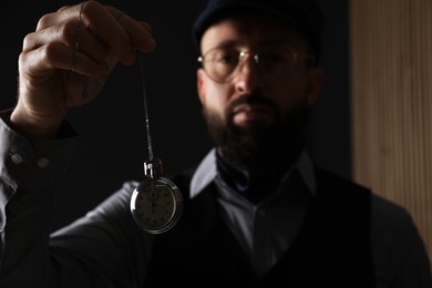 Photo of Hypnosis session. Man swinging vintage pocket watch indoors, selective focus