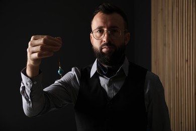 Photo of Hypnosis session. Man in glasses swinging pendulum indoors