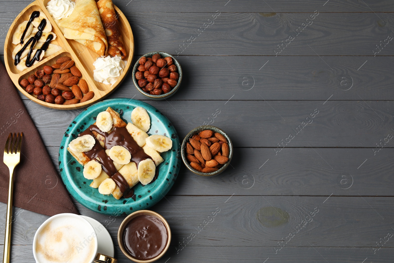 Photo of Delicious crepes served with chocolate paste, nuts and coffee on grey wooden table, flat lay. Space for text