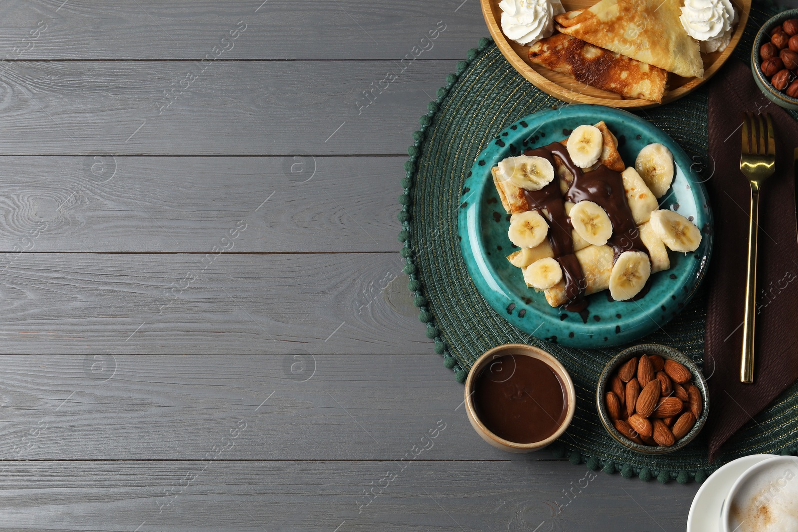 Photo of Delicious crepes served with chocolate paste, nuts and coffee on grey wooden table, flat lay. Space for text