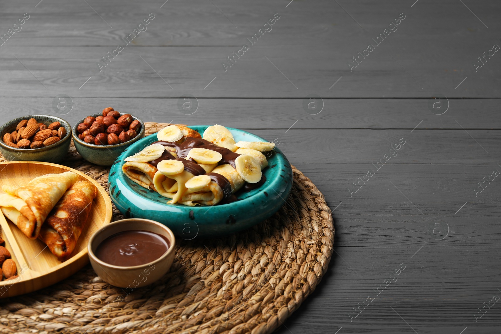 Photo of Delicious crepes served with chocolate paste and nuts on grey wooden table, space for text