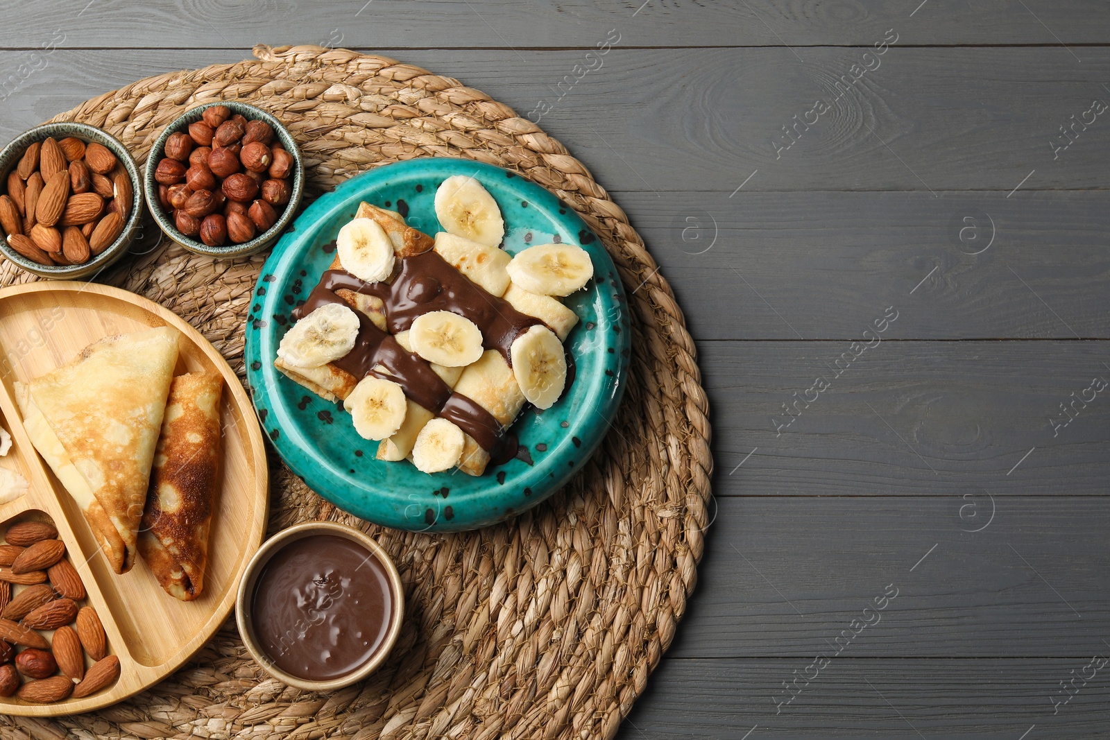 Photo of Delicious crepes served with chocolate paste and nuts on grey wooden table, flat lay. Space for text