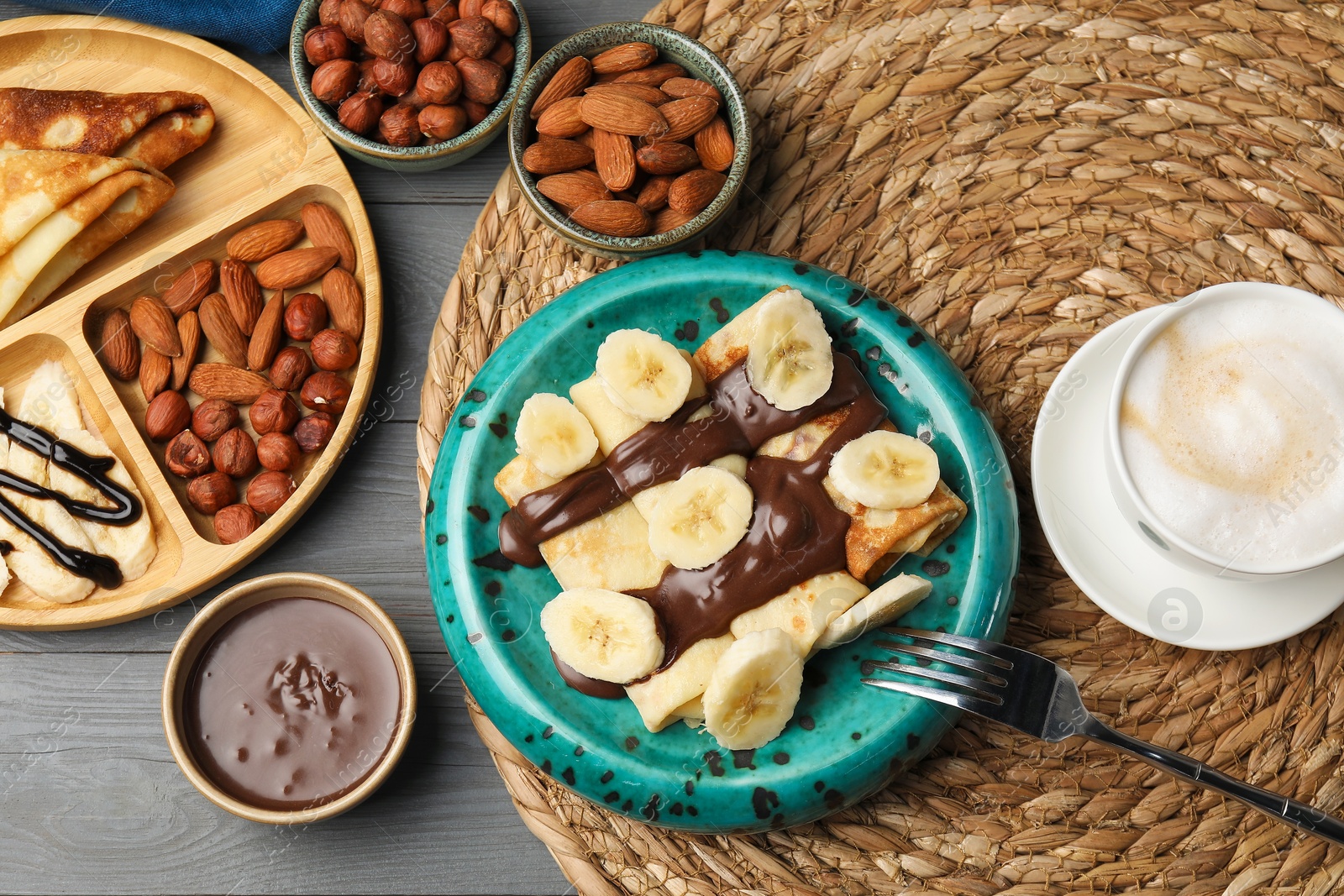 Photo of Delicious crepes served with chocolate paste, nuts and coffee on grey wooden table, flat lay