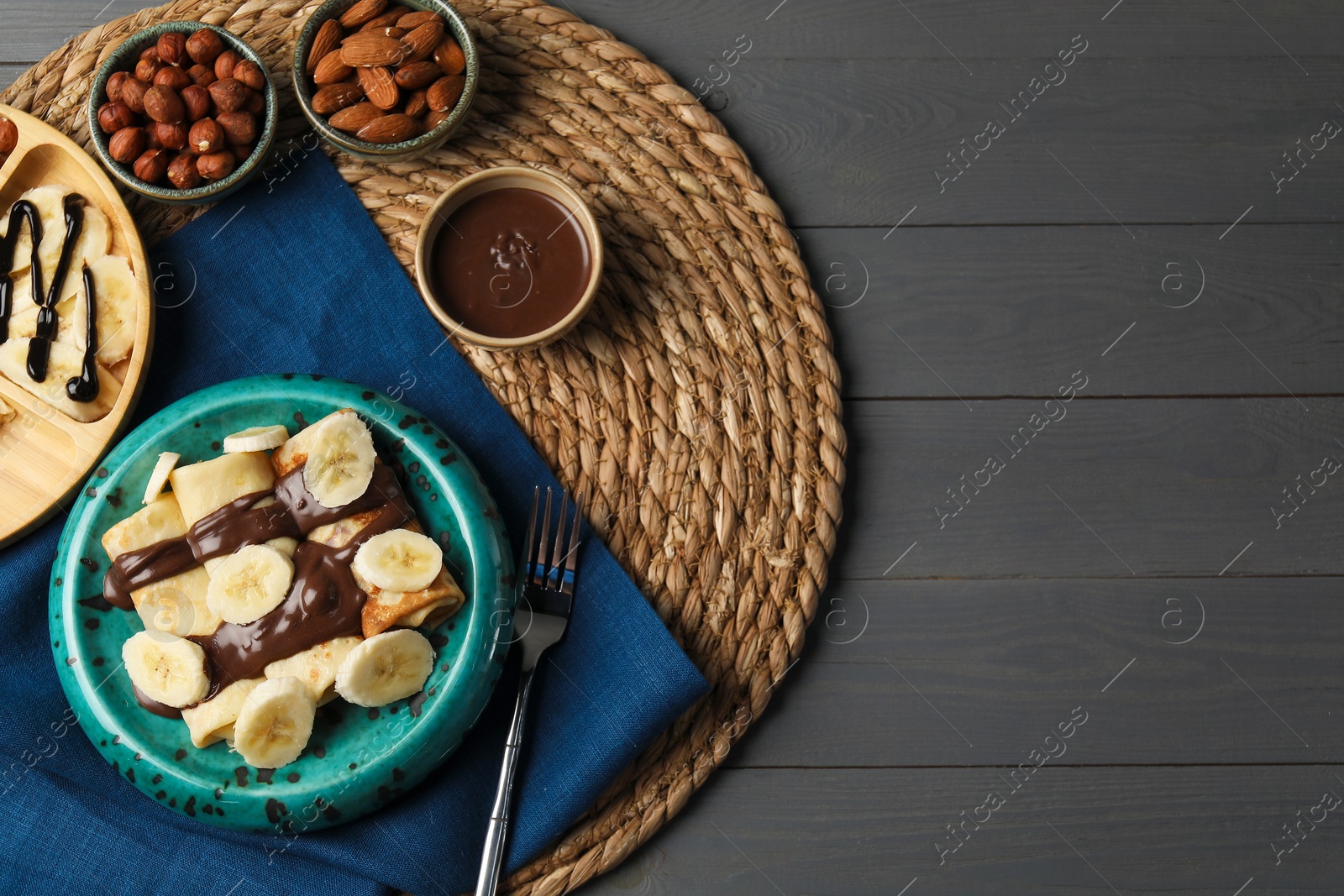 Photo of Delicious crepes served with chocolate paste and nuts on grey wooden table, flat lay. Space for text