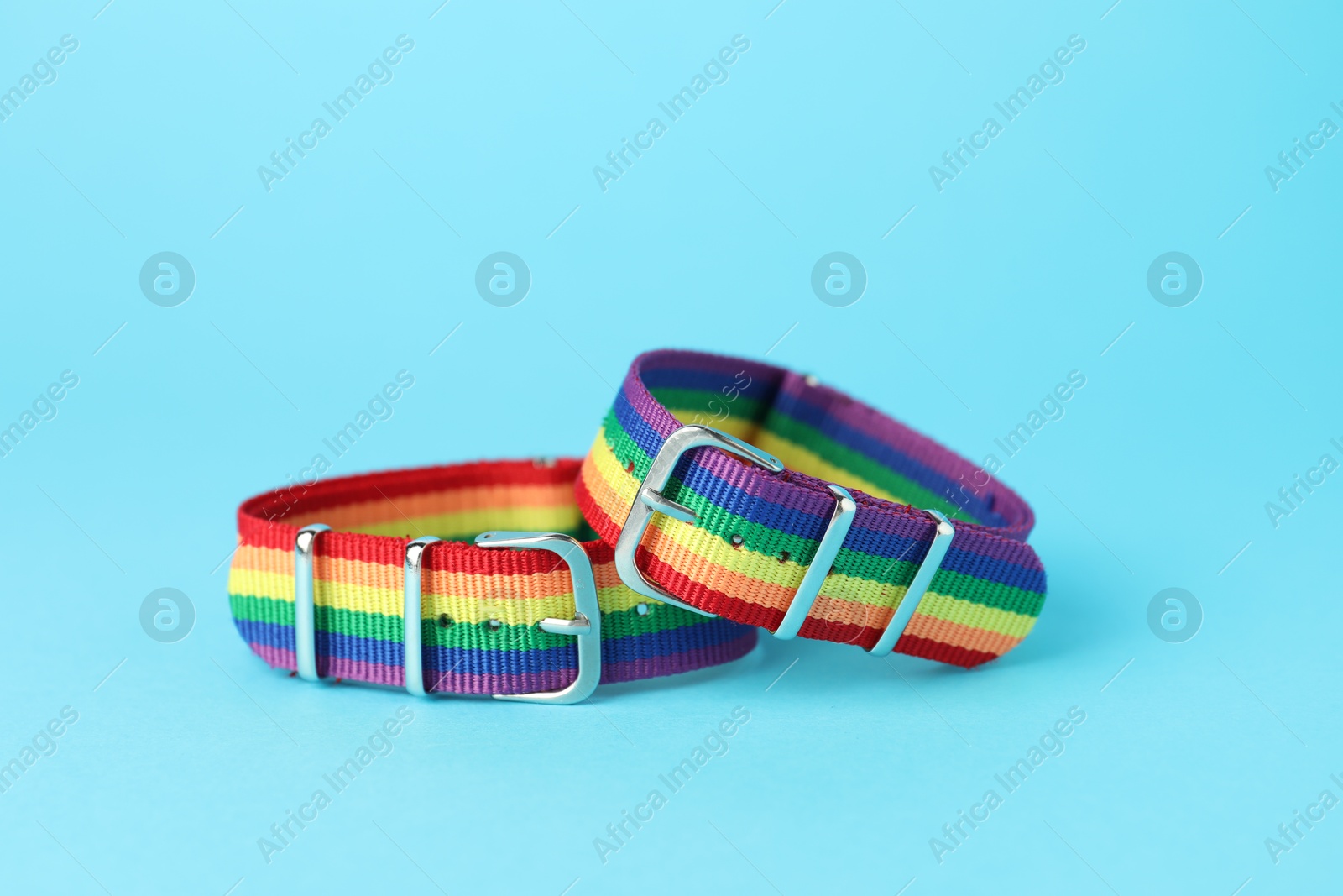 Photo of Two wristbands in LGBT colors on light blue background, closeup