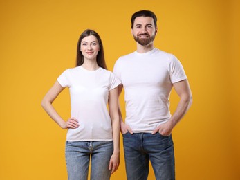 Photo of Woman and man wearing blank white t-shirts on orange background. Mockup for design