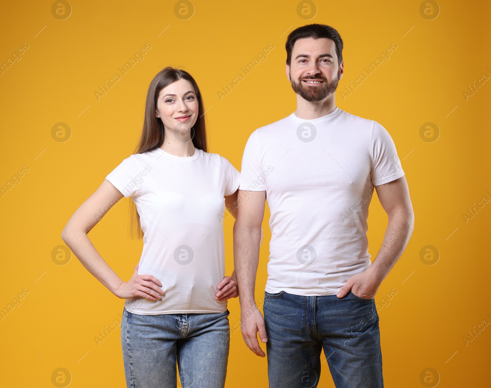 Photo of Woman and man wearing blank white t-shirts on orange background. Mockup for design