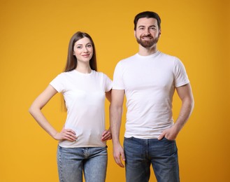 Woman and man wearing blank white t-shirts on orange background. Mockup for design