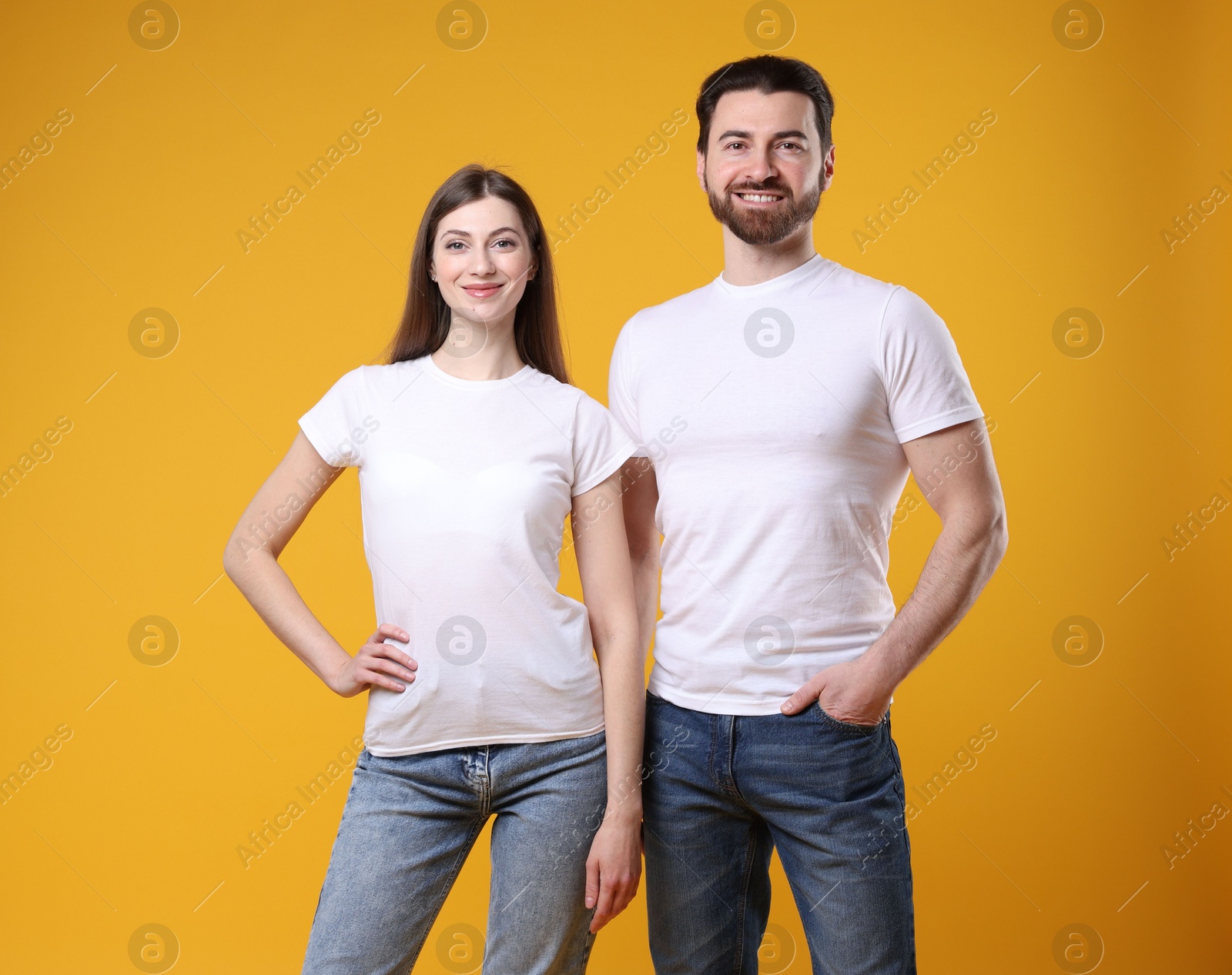 Photo of Woman and man wearing blank white t-shirts on orange background. Mockup for design