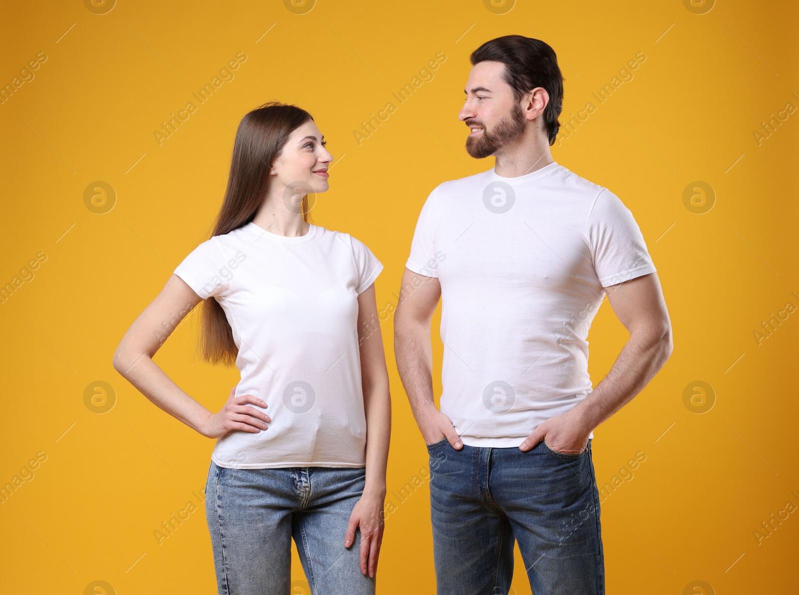 Photo of Woman and man wearing blank white t-shirts on orange background. Mockup for design