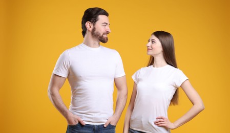 Photo of Woman and man wearing blank white t-shirts on orange background. Mockup for design