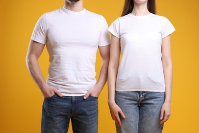 Photo of Woman and man wearing blank white t-shirts on orange background, closeup. Mockup for design