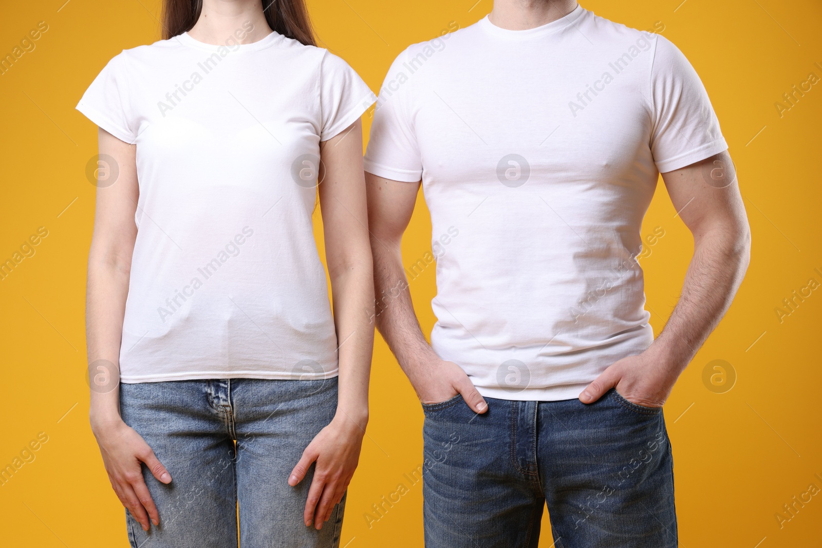 Photo of Woman and man wearing blank white t-shirts on orange background, closeup. Mockup for design