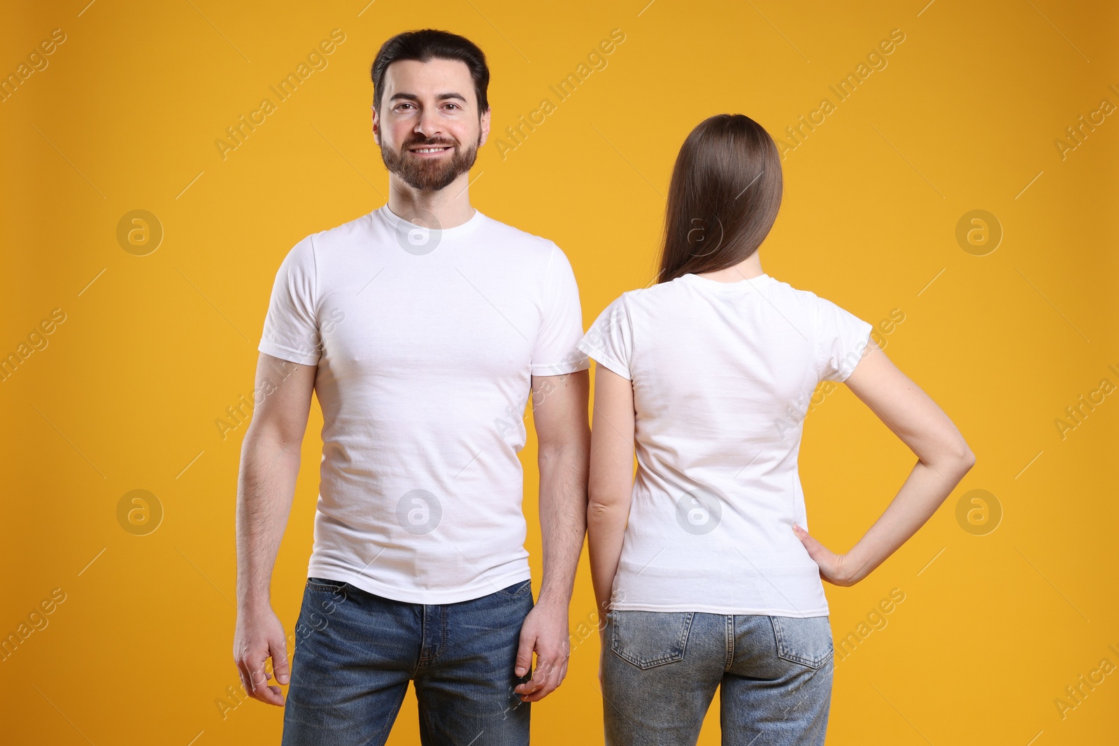 Photo of Woman and man wearing blank white t-shirts on orange background. Mockup for design