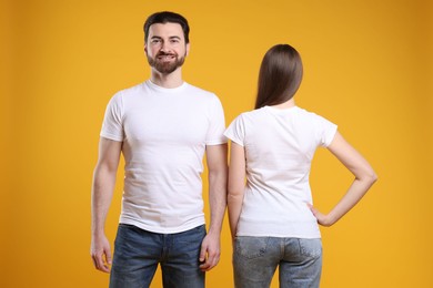 Photo of Woman and man wearing blank white t-shirts on orange background. Mockup for design