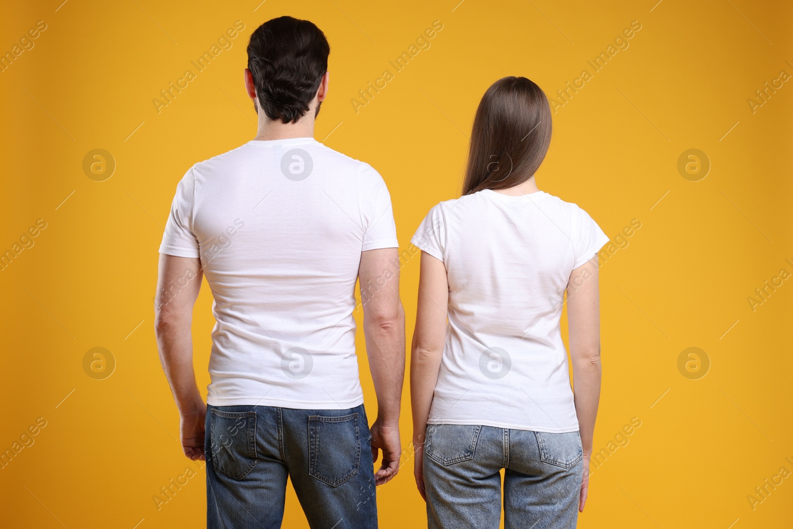 Photo of Woman and man wearing blank white t-shirts on orange background, back view. Mockup for design