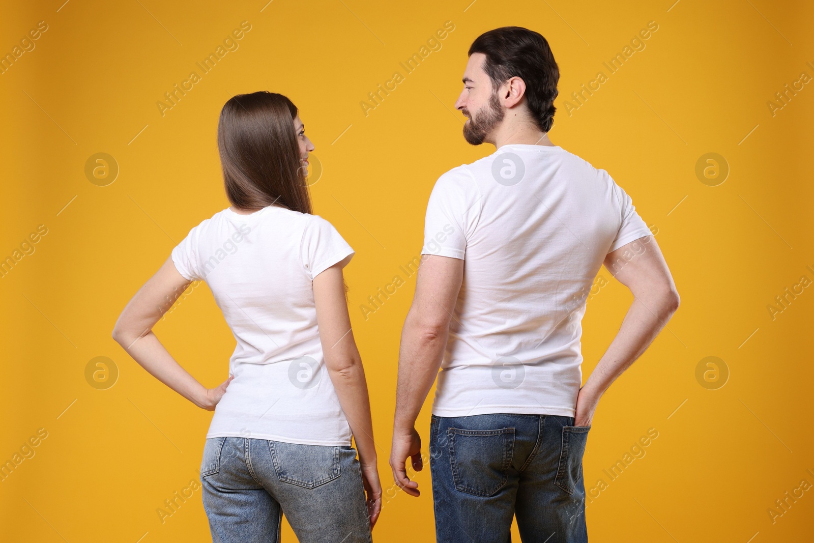 Photo of Woman and man wearing blank white t-shirts on orange background, back view. Mockup for design