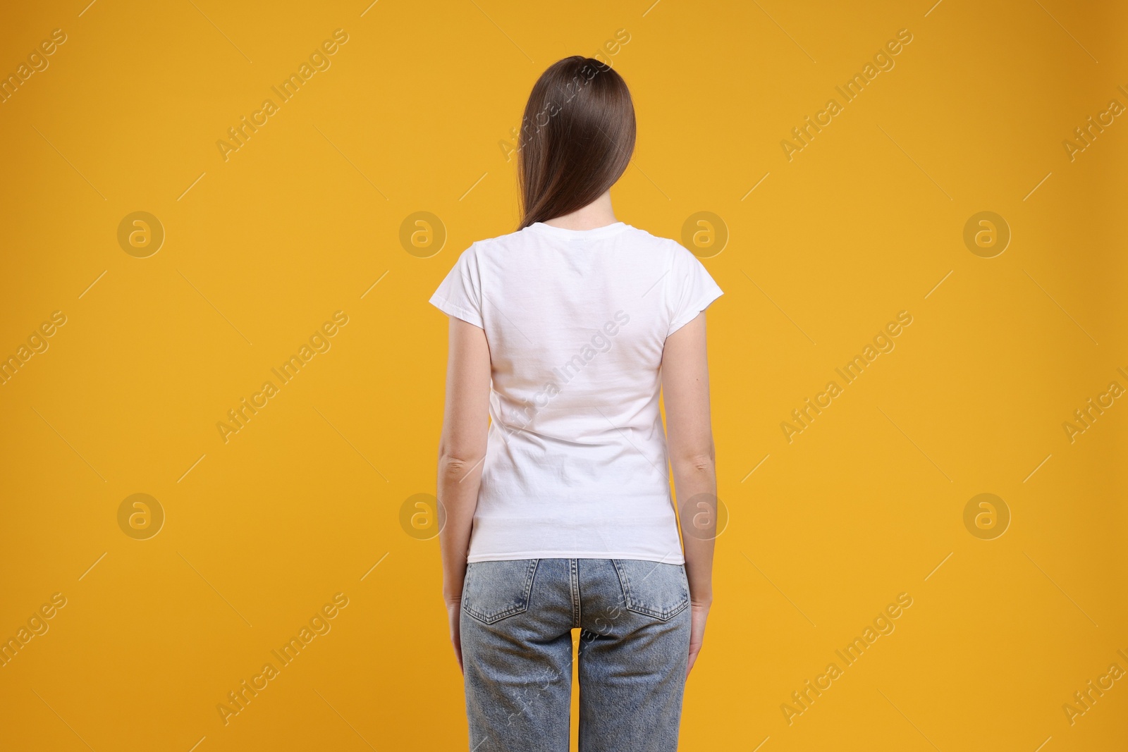 Photo of Woman wearing blank white t-shirt on orange background, back view. Mockup for design