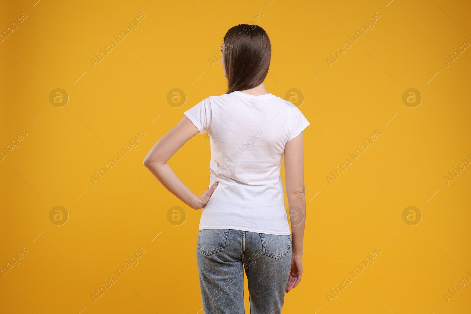 Photo of Woman wearing blank white t-shirt on orange background, back view. Mockup for design