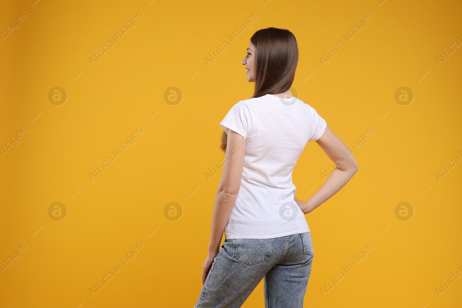 Photo of Woman wearing blank white t-shirt on orange background, back view. Mockup for design