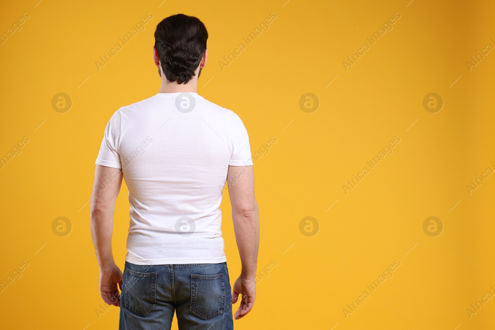 Photo of Man wearing blank white t-shirt on orange background, back view. Mockup for design