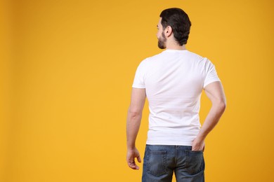 Photo of Man wearing blank white t-shirt on orange background, back view. Mockup for design