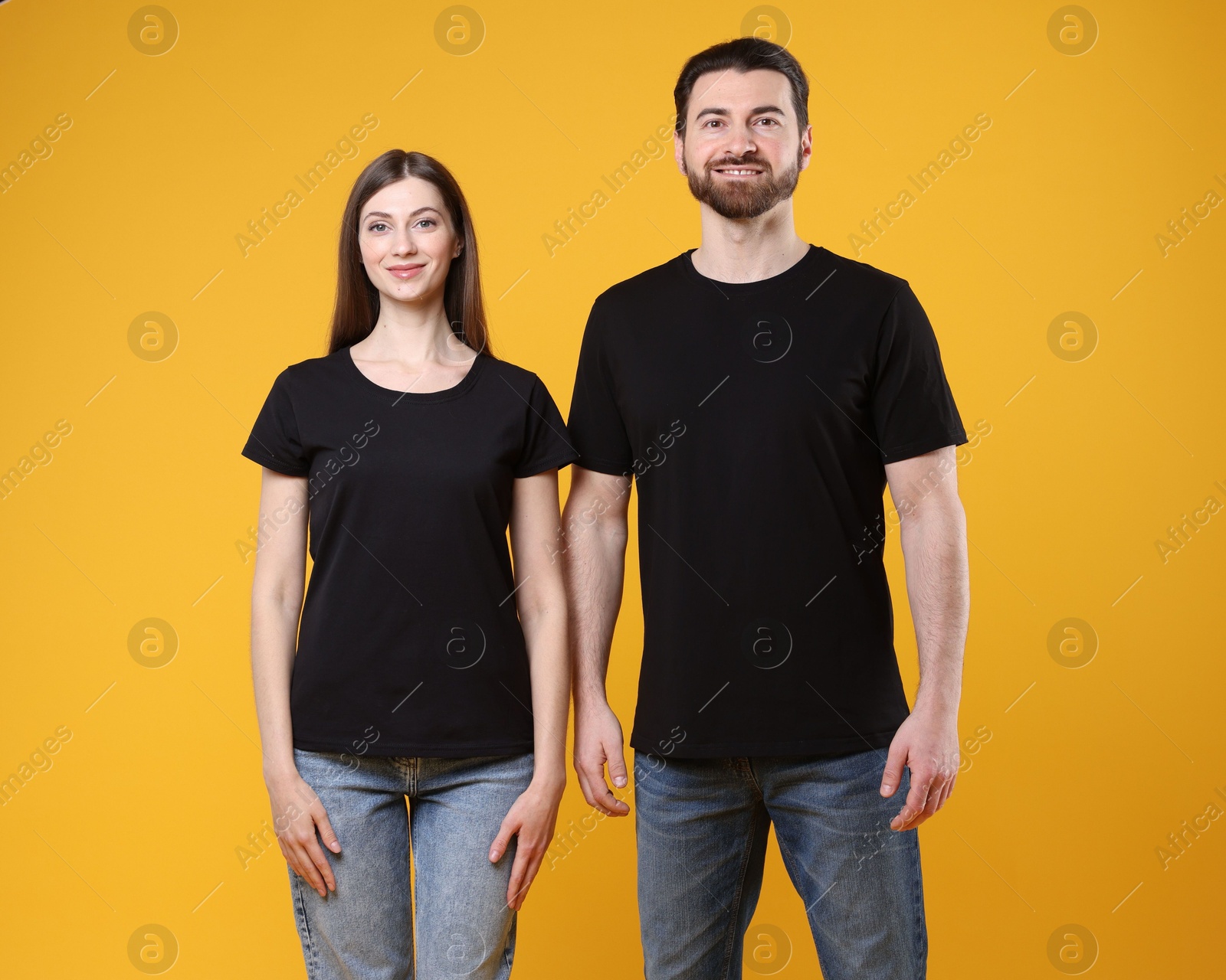 Photo of Woman and man wearing blank black t-shirts on orange background. Mockup for design