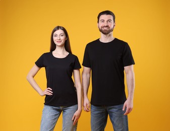 Photo of Woman and man wearing blank black t-shirts on orange background. Mockup for design