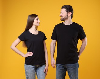 Photo of Woman and man wearing blank black t-shirts on orange background. Mockup for design