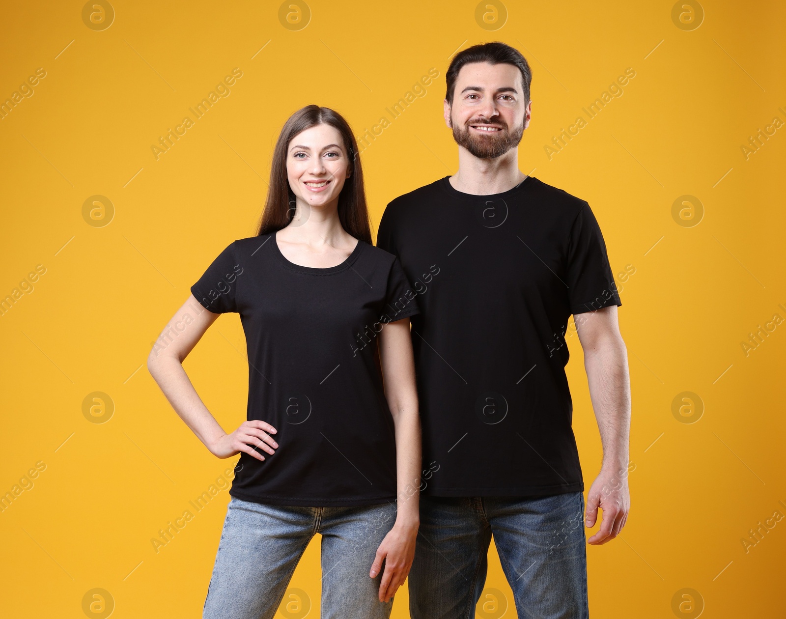 Photo of Woman and man wearing blank black t-shirts on orange background. Mockup for design