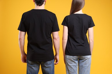 Photo of Woman and man wearing blank black t-shirts on orange background, back view. Mockup for design