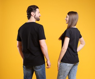 Photo of Woman and man wearing blank black t-shirts on orange background, back view. Mockup for design