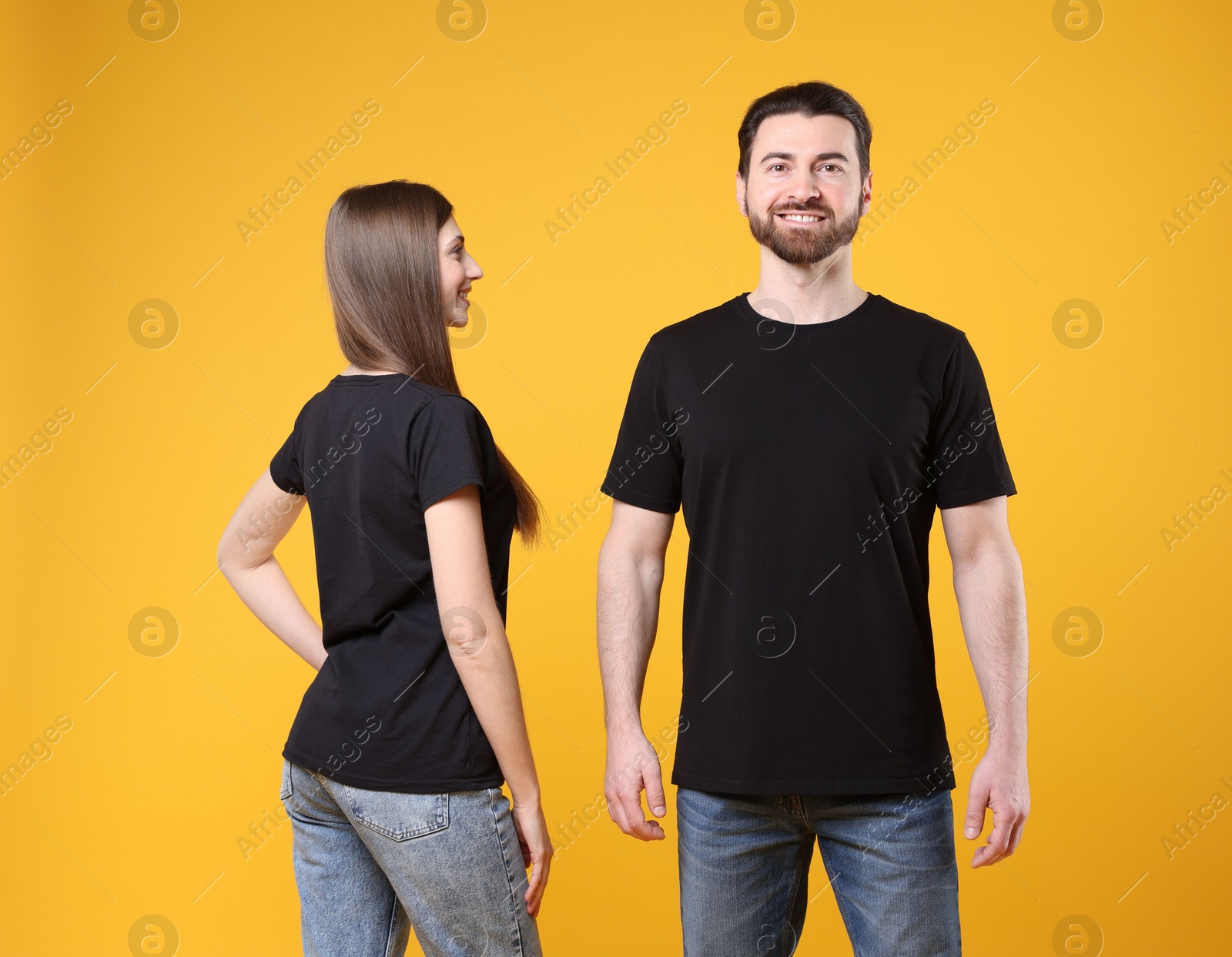 Photo of Woman and man wearing blank black t-shirts on orange background. Mockup for design