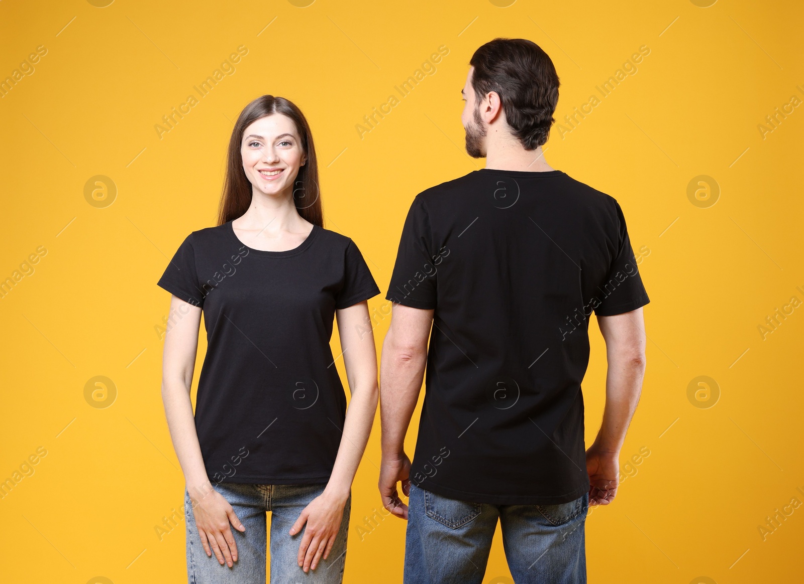 Photo of Woman and man wearing blank black t-shirts on orange background. Mockup for design