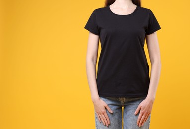 Photo of Woman wearing blank black t-shirt on orange background, closeup. Mockup for design