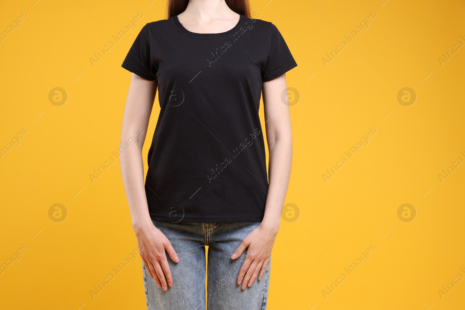 Photo of Woman wearing blank black t-shirt on orange background, closeup. Mockup for design