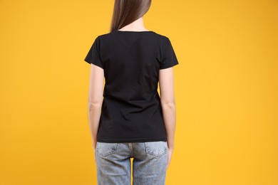 Photo of Woman wearing blank black t-shirt on orange background, back view. Mockup for design