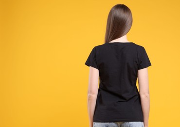 Photo of Woman wearing blank black t-shirt on orange background, back view. Mockup for design