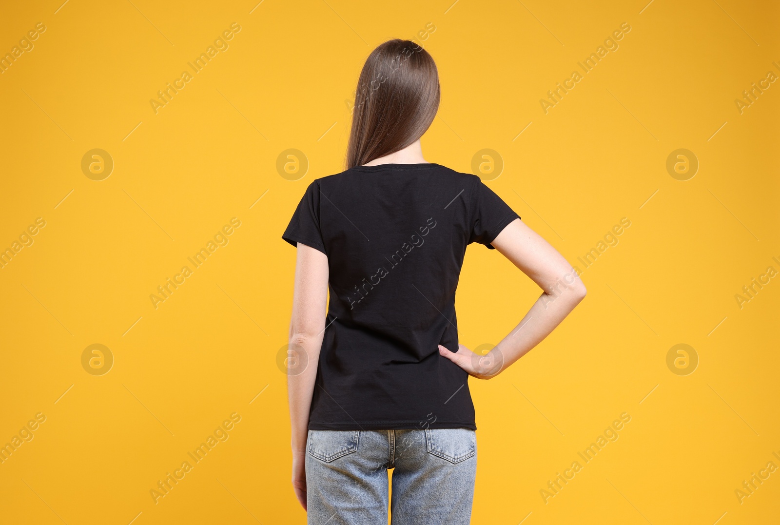 Photo of Woman wearing blank black t-shirt on orange background, back view. Mockup for design