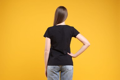 Photo of Woman wearing blank black t-shirt on orange background, back view. Mockup for design