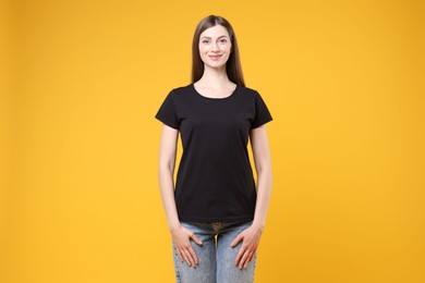 Photo of Woman wearing blank black t-shirt on orange background. Mockup for design