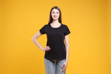 Photo of Woman wearing blank black t-shirt on orange background. Mockup for design