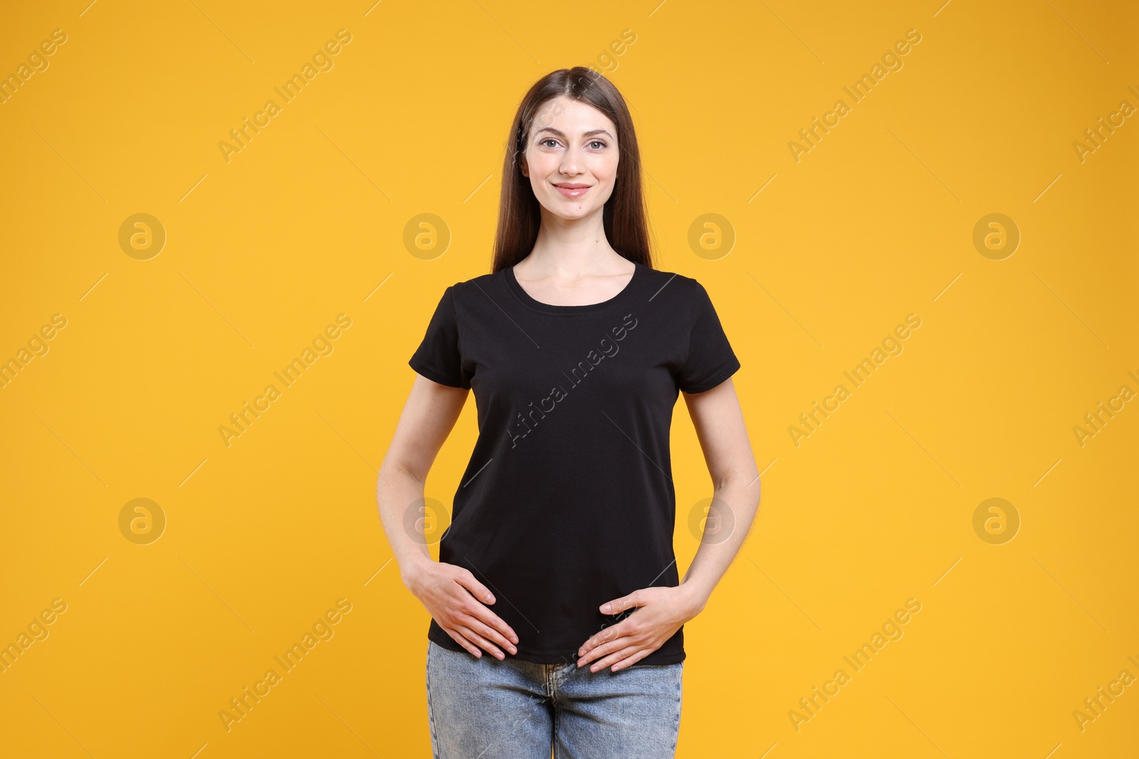 Photo of Woman wearing blank black t-shirt on orange background. Mockup for design