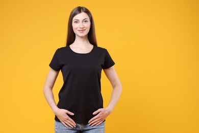 Photo of Woman wearing blank black t-shirt on orange background. Mockup for design