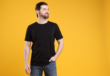 Photo of Man wearing blank black t-shirt on orange background. Mockup for design