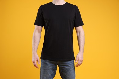 Photo of Man wearing blank black t-shirt on orange background, closeup. Mockup for design